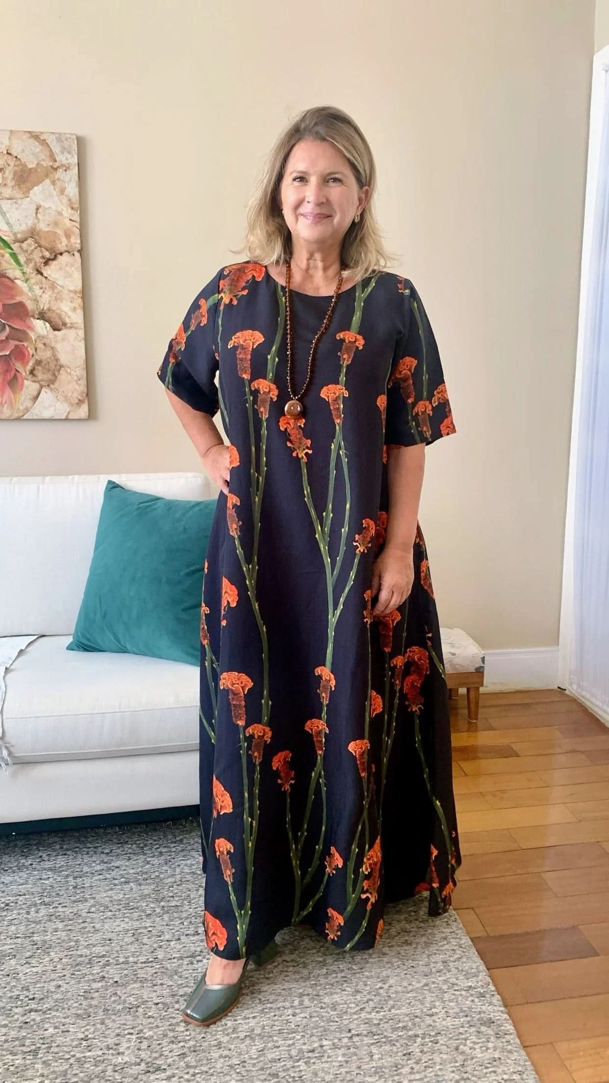 Mulher usando vestido maxi floral preto com flores laranjas em ambiente residencial elegante EZILDINHA