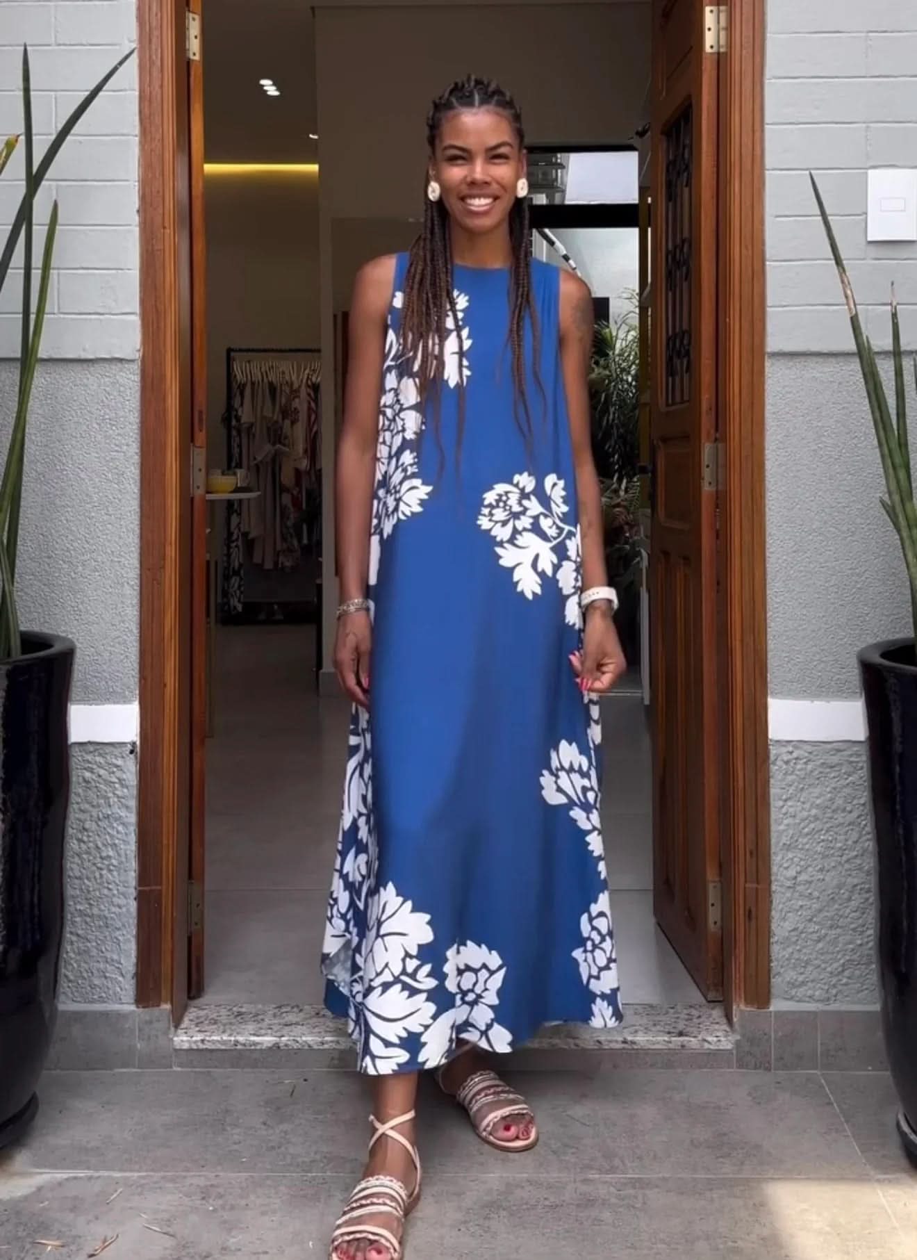 Mulher sorrindo usa vestido regata azul com estampa floral branca em frente à loja EZILDINHA