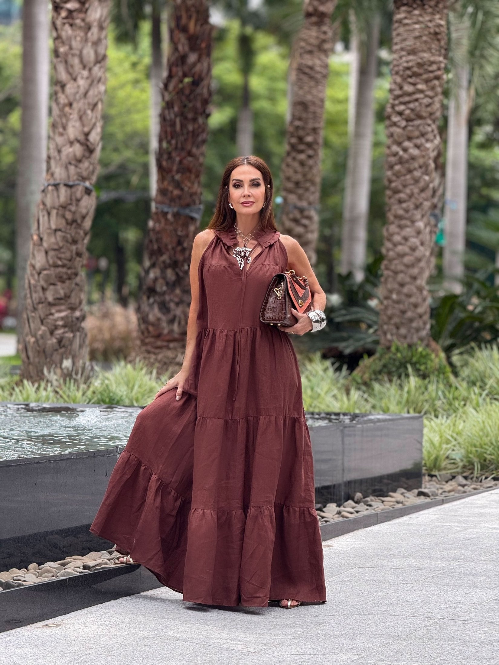 Mulher usando vestido longo de linho puro marrom, ao ar livre perto de palmeiras EZILDINHA