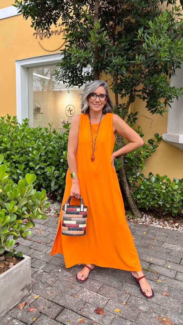 Mulher usando vestido longo laranja de linho, bolsa colorida, acessórios, em área externa elegante EZILDINHA