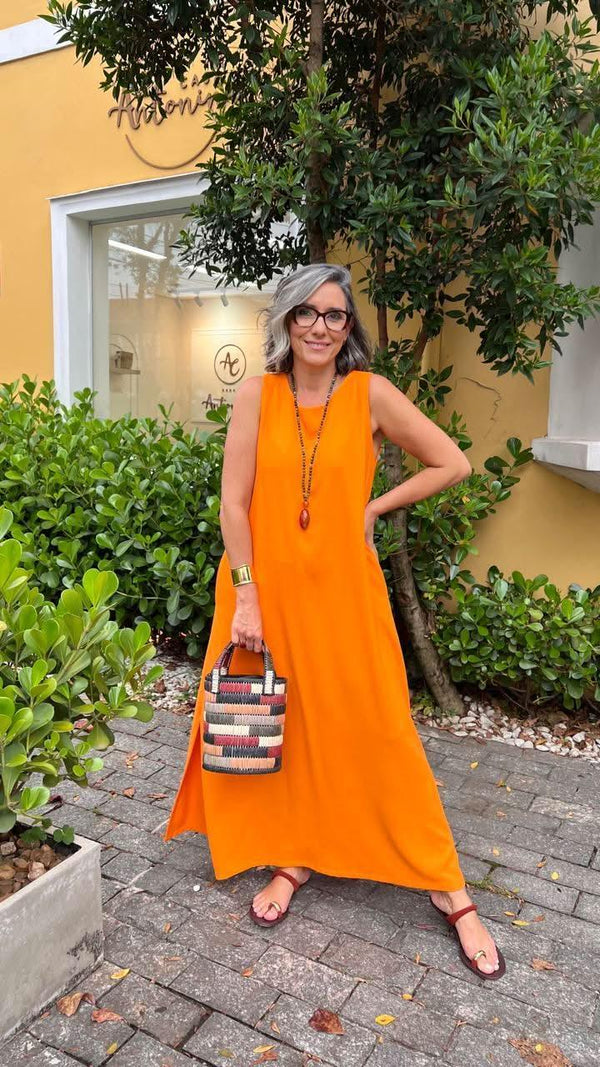 Mulher usando vestido longo laranja de linho, bolsa colorida, acessórios, em área externa elegante EZILDINHA