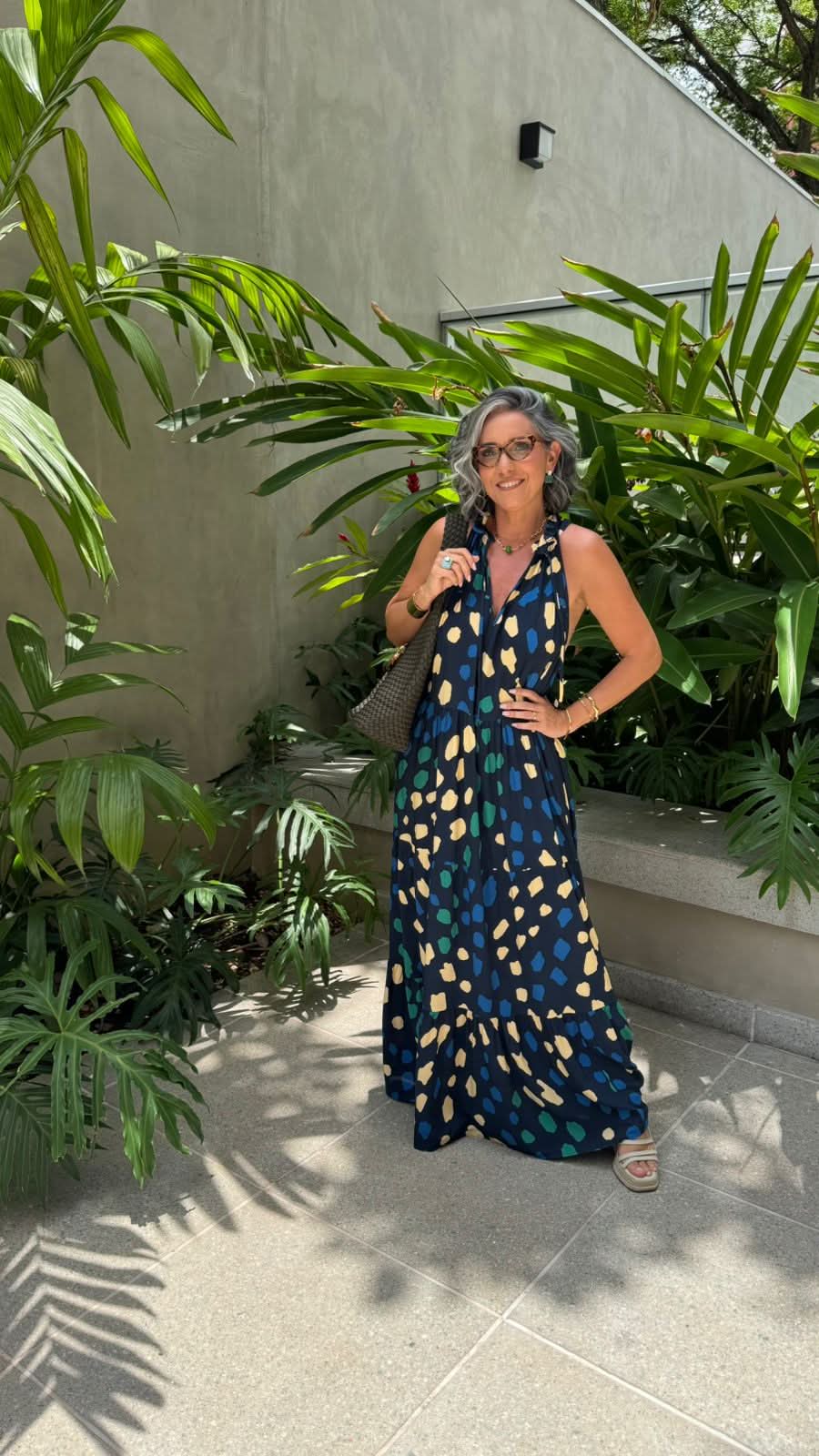 Mulher sorrindo com vestido longo estampado em fundo de plantas tropicais ao ar livre EZILDINHA