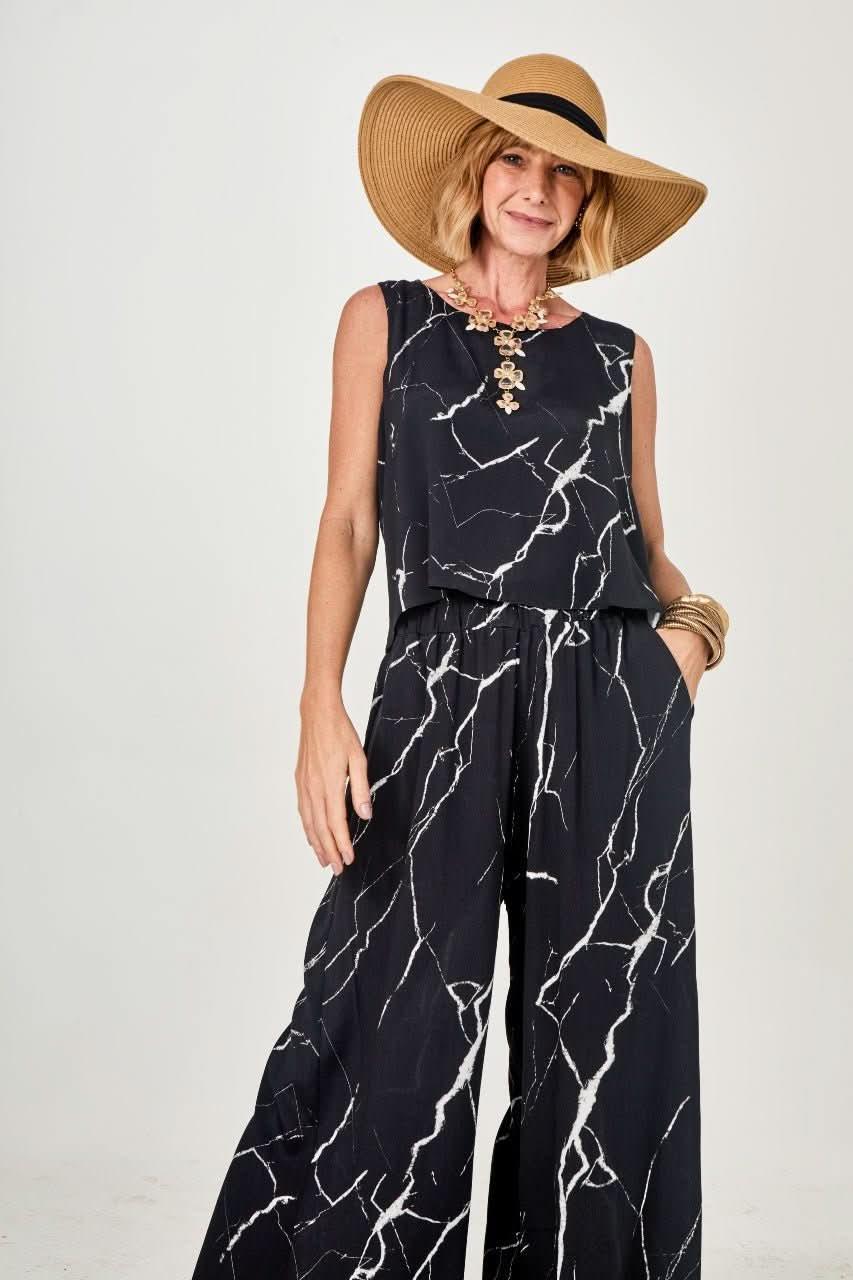 Mulher usando conjunto preto com estampa marmorizada, chapéu de palha e acessórios EZILDINHA