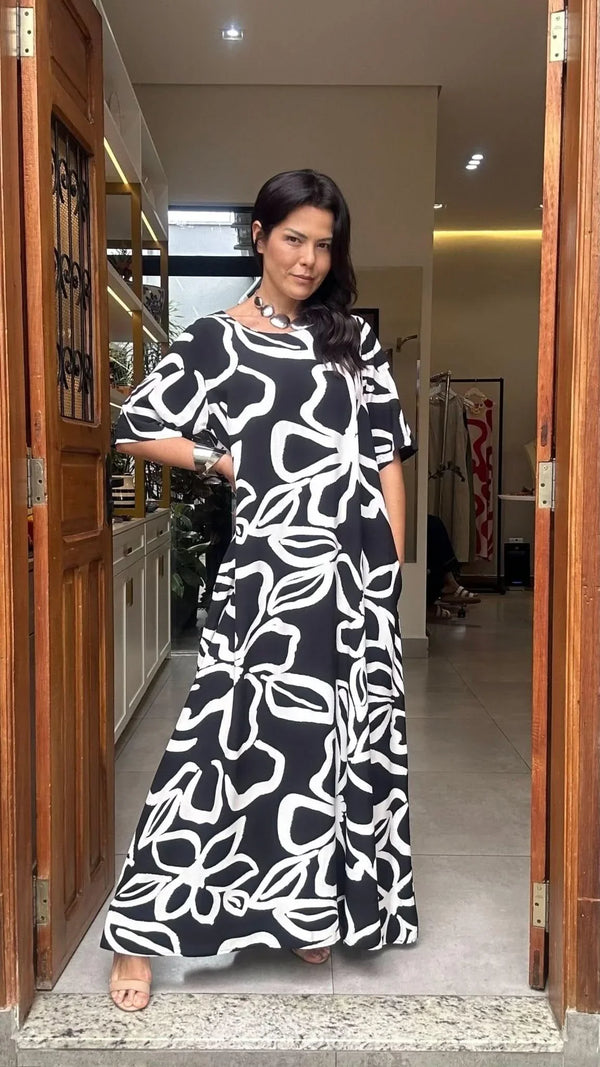 Mulher usando vestido longo preto com estampa floral branca, em ambiente interno elegante EZILDINHA