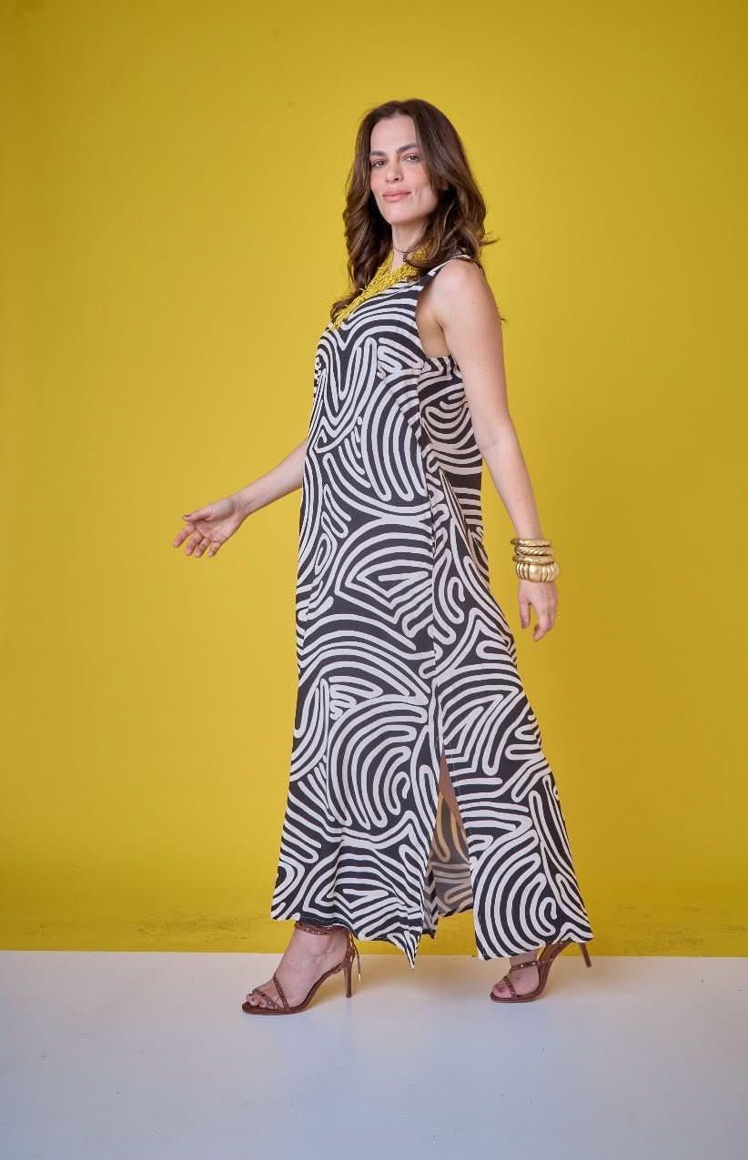 Mulher usando vestido longo de linho preto e branco com estampa de linhas, fundo amarelo EZILDINHA