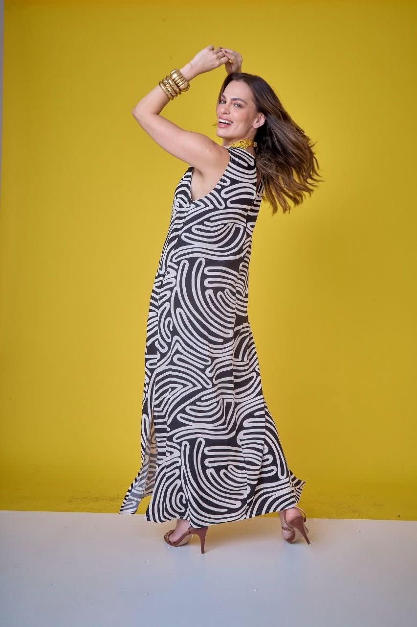 Mulher usando vestido longo preto e branco com estampa geométrica em fundo amarelo EZILDINHA