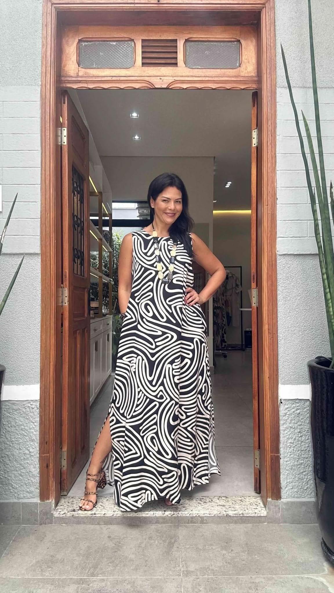 Mulher usando vestido longo preto e branco com estampa de linhas, em porta de entrada elegante EZILDINHA
