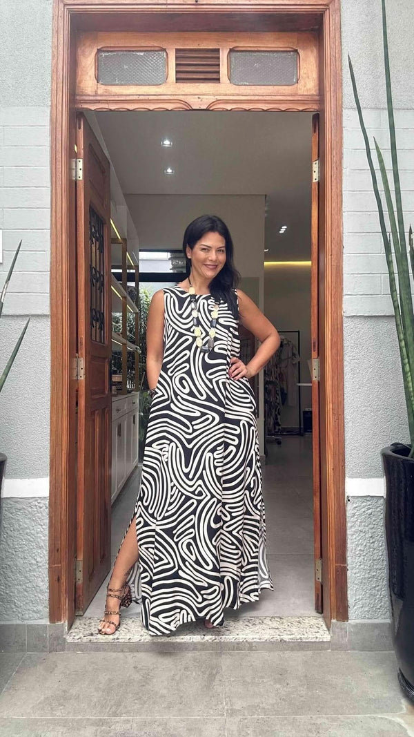 Mulher usando vestido longo preto e branco com estampa de linhas, em porta de entrada elegante EZILDINHA