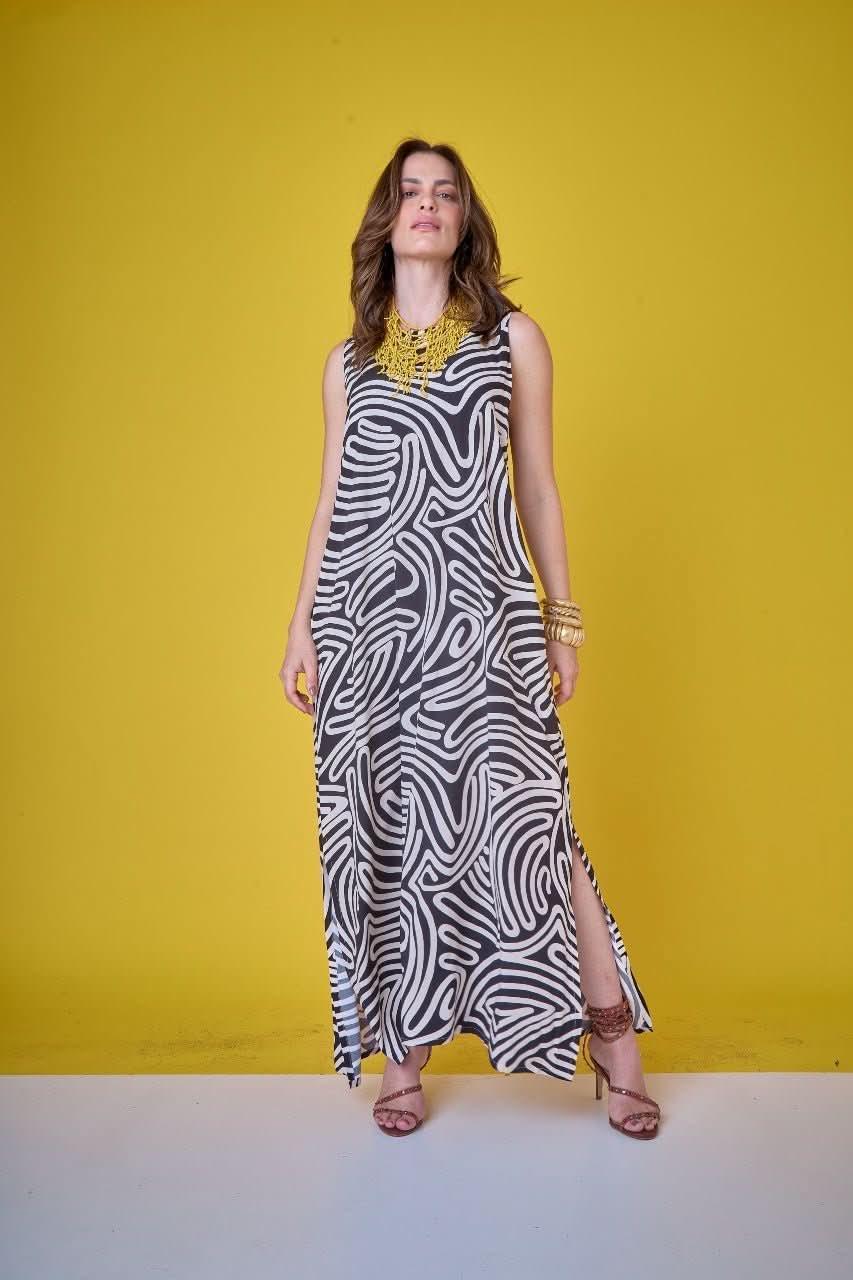 Mulher vestindo vestido longo preto e branco com estampa geométrica, fundo amarelo EZILDINHA