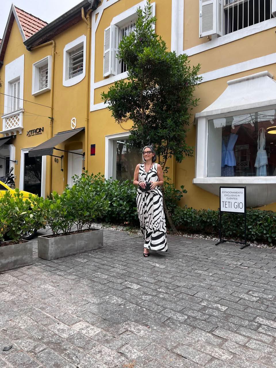 Mulher com vestido longo estampa preta e branca, em frente a prédio amarelo elegante EZILDINHA