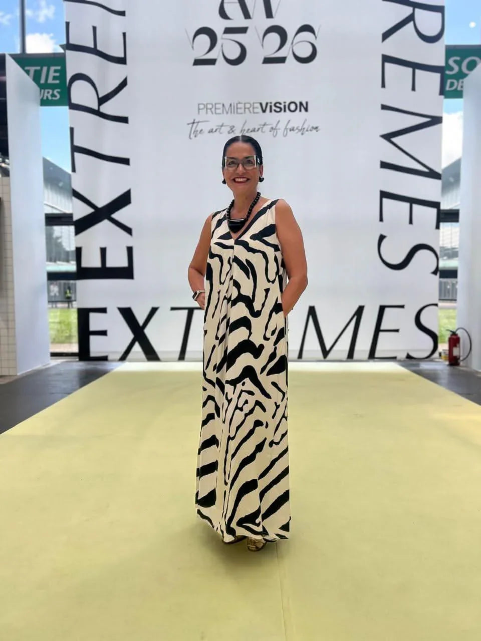 Mulher usando vestido longo estampado preto e branco em evento de moda, passarela interna iluminada EZILDINHA