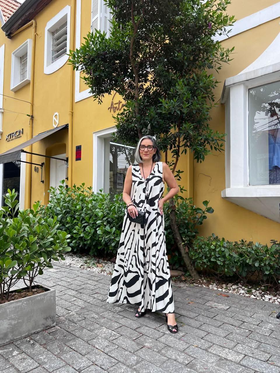 Mulher usando vestido longo preto e branco com estampa abstrata, ao ar livre em frente a prédio amarelo EZILDINHA