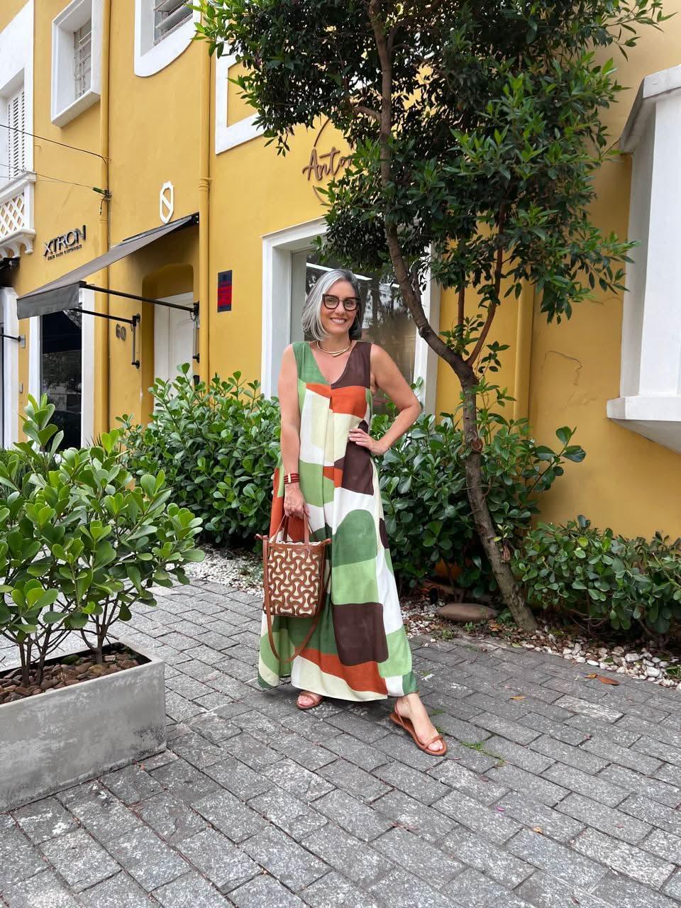 Mulher com vestido longo estampado verde, marrom e laranja, bolsa de couro, ao ar livre EZILDINHA