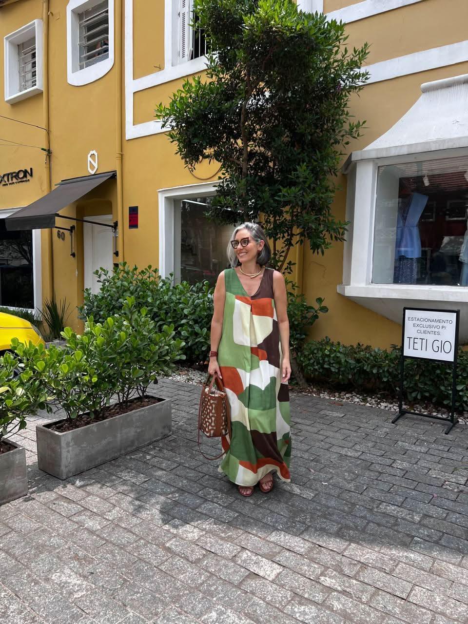 Mulher usando vestido longo estampado geométrico verde, marrom e laranja em ambiente urbano EZILDINHA