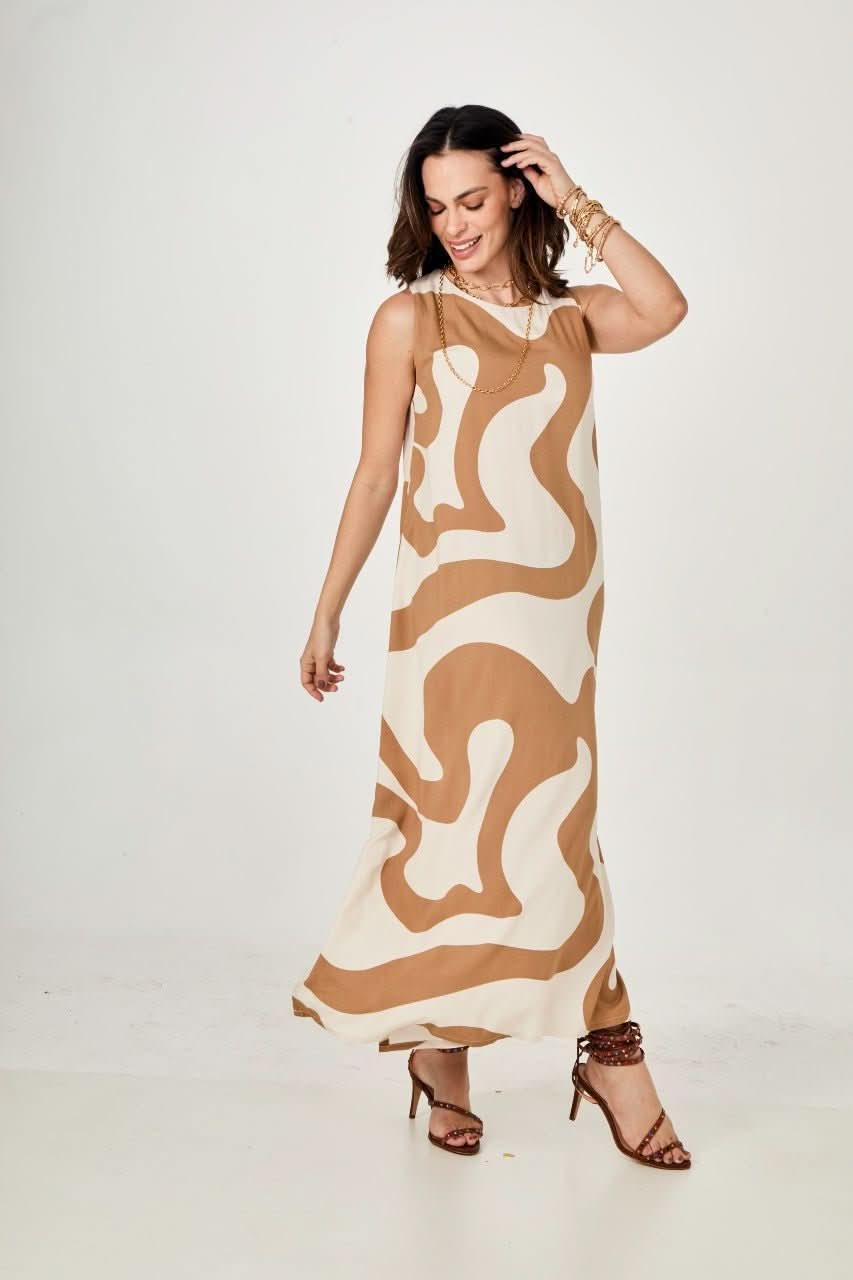 Mulher vestindo vestido longo bege com estampa ondulada, sandálias de salto, fundo branco EZILDINHA