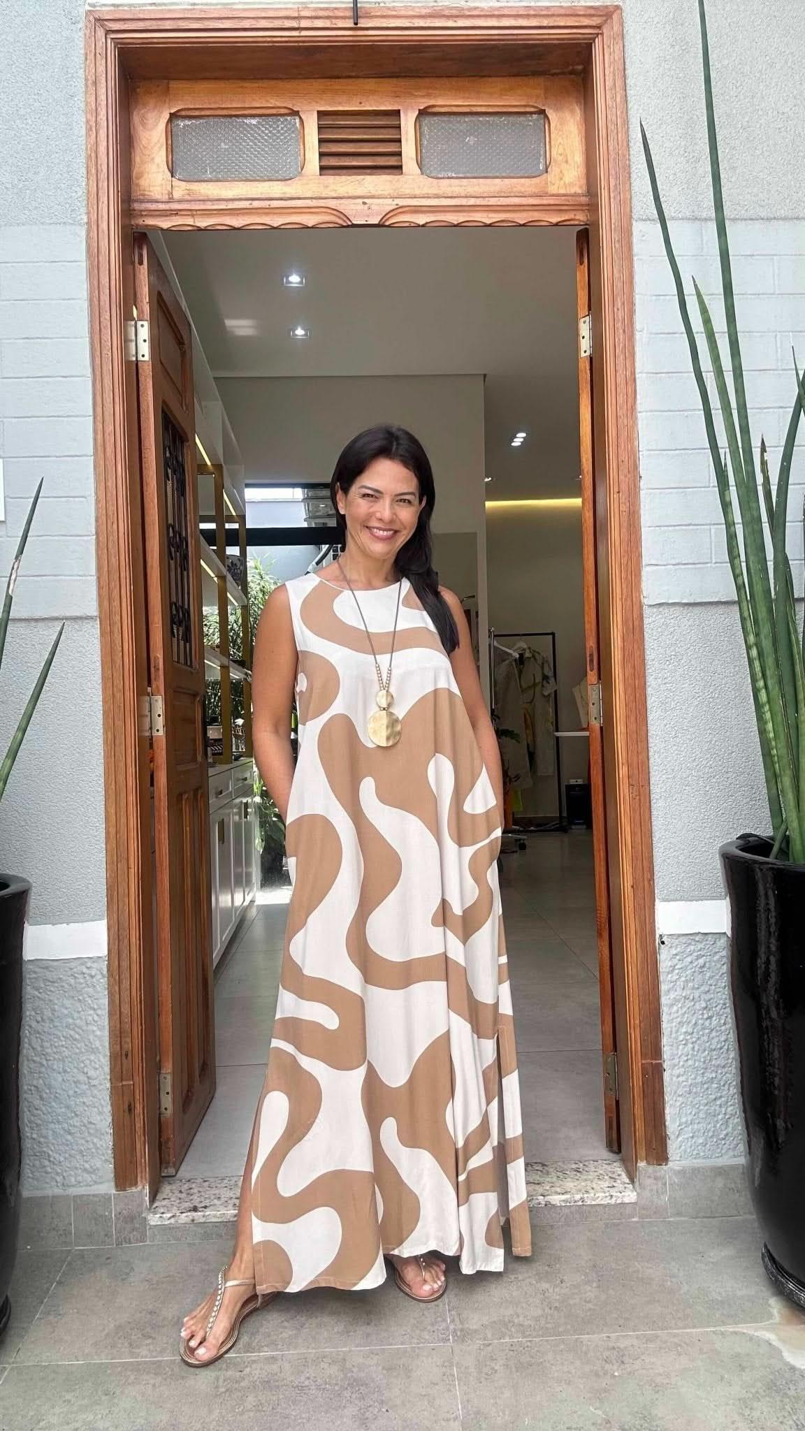 Mulher usando vestido longo bege com estampa ondulada, em frente a porta de madeira, estilo casual elegante EZILDINHA
