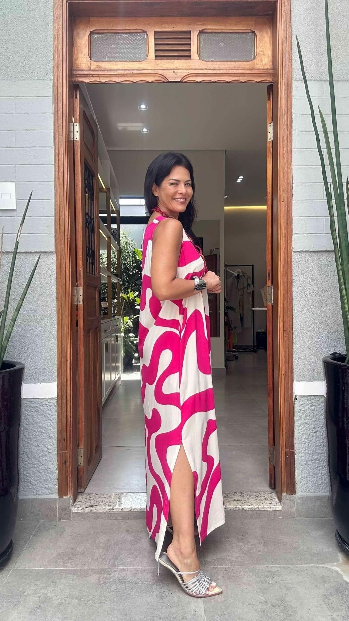Mulher usando vestido longo branco com estampa pink e fenda, em porta de entrada elegante EZILDINHA